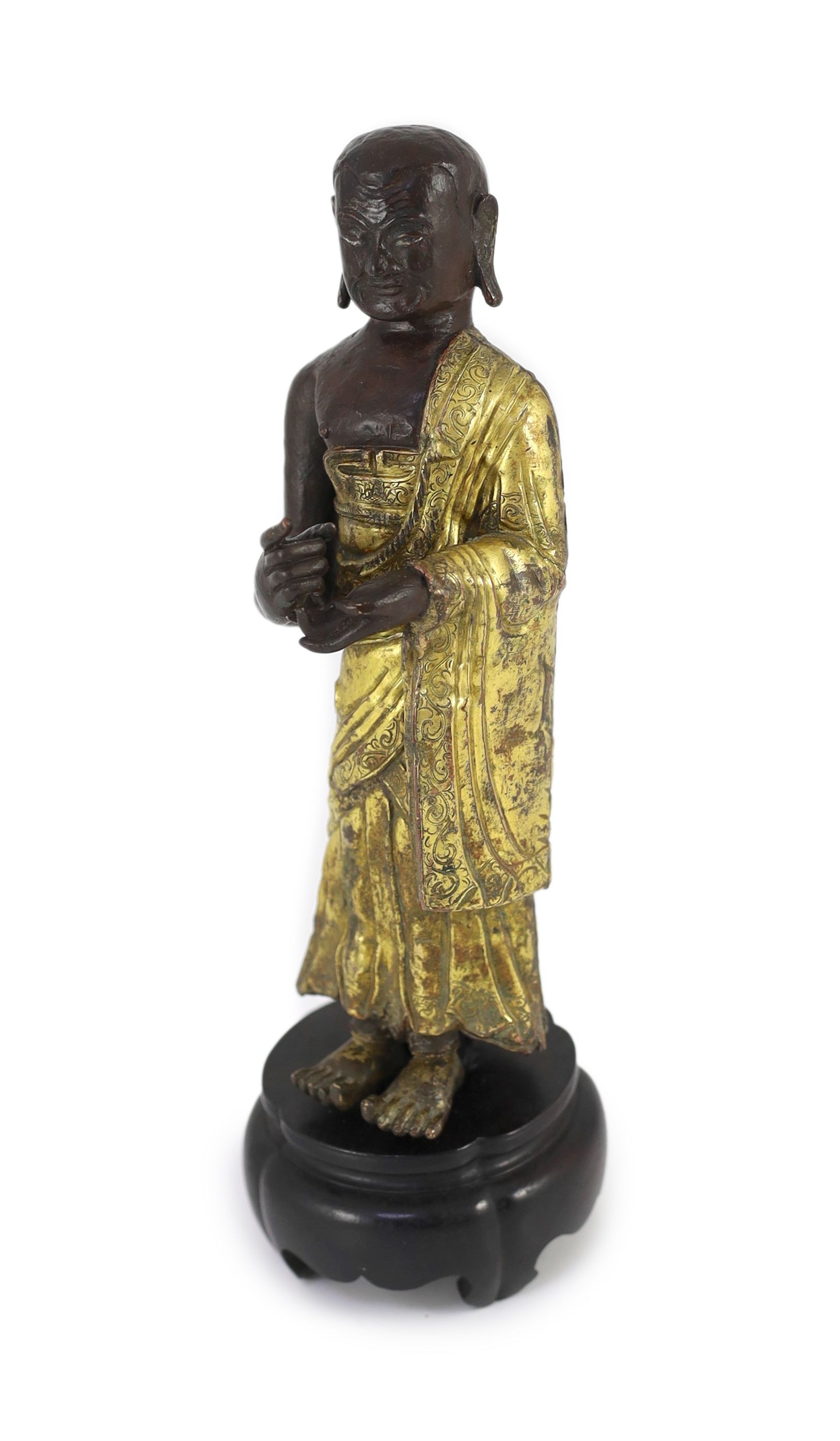 A Tibetan repousse work gilt and lacquered copper figure of a luohan, 18th century, 20.5 cm high, wood stand